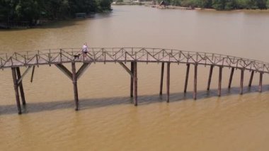 Siyah köpeği olan çekici genç bir kadın köprüden geçiyor. Chumphon, Tayland 'daki Nong Yai Pond ve Tahta Köprüsü' nün 4K yavaş çekim videosu..