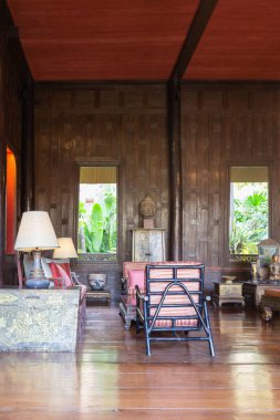 Ahşap duvarları ve mobilyaları olan, Jim Thompson Evi, Bangkok, Tayland 'da bir avize, oturma alanı ve Buda heykeli bulunan güzel dekore edilmiş geleneksel bir Tayland iç mimarisi.