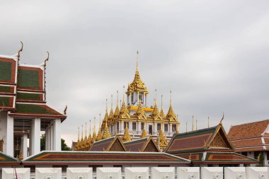 Wat Ratchanatdaram 'daki Loha Prasat tapınağı, Bangkok, Tayland, görkemli altın kuleleri ve karmaşık Tayland mimarisi, bulutlu bir gökyüzüne karşı kurulmuş.