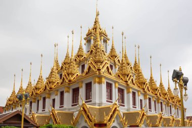 Wat Ratchanatdaram 'daki Loha Prasat tapınağı, Bangkok, Tayland, görkemli altın kuleleri ve karmaşık Tayland mimarisi, bulutlu bir gökyüzüne karşı kurulmuş.