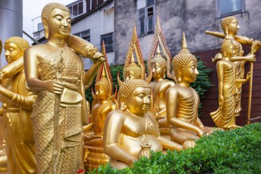 Golden Buddha statues at Wat Ratchanatdaram, Bangkok, Thailand. Various postures and expressions, intricate details, lush greenery clipart