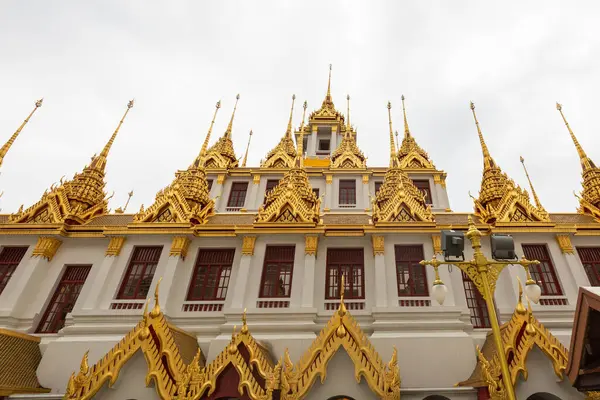 Stock image Loha Prasat temple in Wat Ratchanatdaram, Bangkok, Thailand, with its majestic golden spires and intricate Thai architecture, set against a cloudy sky