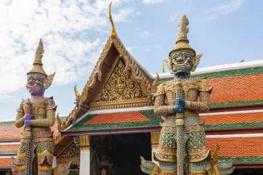 Güneşli bir günde Bangkok, Tayland 'da mavi gökyüzüne karşı koruyucu heykellerle çevrili Zümrüt Buddha Tapınağı' nın zengin süslü kapıları.