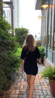 Bir kız nehir kenarında yürüyor, gün batımında bulutlu gökyüzüne bakıyor, Bangkok, Tayland 'da sakin ve düşünceli bir anı yakalıyor. Bangkok, Tayland - 30 Ekim 2023.