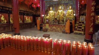 Turuncu cüppeli keşişler, altın Buda heykelleriyle süslenmiş bir tapınakta ayin yapıyorlar. Ön planda yanan mum sıraları parlıyor. Bangkok, Tayland - 25 Ekim 2023.