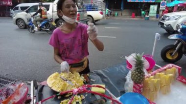 Bangkok 'ta bir sokak satıcısı yol kenarında taze ananas hazırlıyor. Sahne canlı sokak yemekleri kültürünü ve şehirdeki günlük yaşamı yakalıyor. Bangkok, Tayland - 25 Kasım 2023.