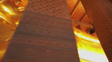 4K videosunda, altın uzanan Buda heykelinin sakin yüzünü ve karmaşık ayrıntılarını vurgulayan bir yakın plan görüntüsü yer alıyor. Sıcak altın rengi, etrafındaki süslü tapınak duvarlarıyla çelişiyor..