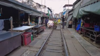 Tedarikçilerin ve yerlilerin derme çatma tezgahlar ve renkli muşambalarla çevrili rayların yakınında etkileşime geçtiği hareketli bir demiryolu sahnesi. Bangkok, Tayland - 30 Ekim 2023.