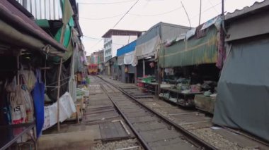 Satıcıların tezgahlarını çabucak ayarladıkları dar bir pazarda renkli bir tren, bu hareketli Tayland demiryolu pazarında ticaret ve ulaşım karışımı. Bangkok, Tayland - 30 Ekim 2023.