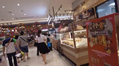 Yemek yiyen ve sosyalleşen insanlarla dolu bir alışveriş merkezindeki yemek salonu. Parlak neon tabelalar ve canlı dekorlar çeşitli yiyecek tezgahlarıyla hareketli bir atmosfer yaratıyor. Bangkok, Tayland - 29 Ekim 2023.