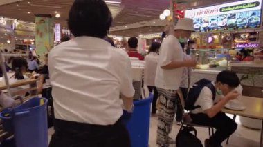 Yemek yiyen ve sosyalleşen insanlarla dolu bir alışveriş merkezindeki yemek salonu. Parlak neon tabelalar ve canlı dekorlar çeşitli yiyecek tezgahlarıyla hareketli bir atmosfer yaratıyor. Bangkok, Tayland - 29 Ekim 2023.