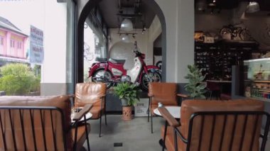 Motosiklet vitrinli, modern koltuklu ve sıcak ışıklandırmalı rahat bir kafe. Özel bir sergi salonu ve günlük yemek alanı karışımı sunuyor. Phuket, Tayland - 05 Kasım 2023.