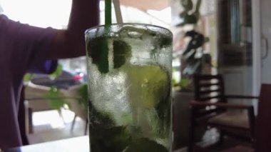 Kireç ve nane yapraklı soğuk, ferahlatıcı bir içeceğin yakın çekimi, yüzeyinde buharlaşma olan bir bardakta servis edilir..