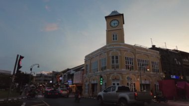 Alacakaranlıkta sarı bir saat kulesinin manzarası. Gökyüzü yumuşak renklerle boyanmış ve aşağıdaki sokakta trafik vardı. Phuket, Tayland - 05 Kasım 2023.