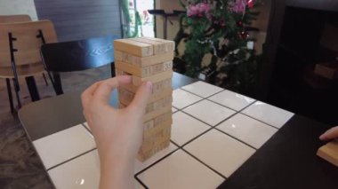 Tahta Jenga kulesine doğru uzanan yakın plan bir el, numaralandırılmış bir bloğu çıkarmaya hazır, Phuket, Tayland 'daki oyunda gerilim yaratıyor..