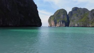 Berrak turkuaz suyu olan yüksek kireçtaşı kayalıklarıyla çevrili sakin bir Maya Körfezi parçalı bulutlu gökyüzüne karşı yerleşerek tropik bir cennetin doğal güzelliklerini yakalıyor..