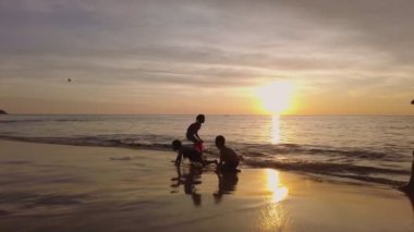 Çocuklar, sakin dalgalar ve ıslak kumdan yansıyan altın ışıkla güzel bir günbatımında sahilde oynamaktan hoşlanırlar. Phuket, Tayland - 15 Kasım 2023.