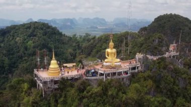 Tayland, Krabi 'deki yemyeşil ormanların ve dramatik kireçtaşı kayalıklarının ortasındaki bir dağın tepesine tünemiş Kaplan Mağarası Tapınağı Wat Tham Suea' daki Altın Buda heykelinin hava manzarası..