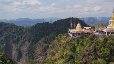 Tayland, Krabi 'deki yemyeşil ormanların ve dramatik kireçtaşı kayalıklarının ortasındaki bir dağın tepesine tünemiş Kaplan Mağarası Tapınağı Wat Tham Suea' daki Altın Buda heykelinin hava manzarası..