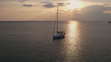 Güneş batarken sakin sularda yüzen sakin bir yelkenli okyanusta altın yansımalar yaratarak huzurlu ve sakin bir manzara yaratıyor..