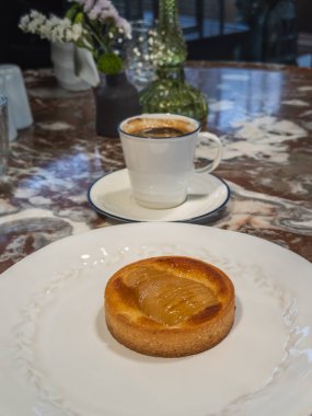 Beyaz tabakta yeni demlenmiş bir fincan kahveyle servis edilen altın armutlu turta, rahat bir kafe havası yaratıyor..