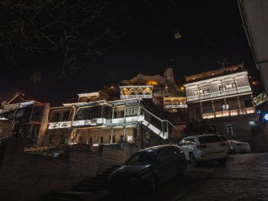 Night view of beautifully illuminated historic buildings with balconies in the Tbilisi old town, showcasing their intricate architecture against a dark sky. clipart