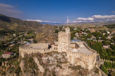 Aerial view of a historic Rabati fortress with stone walls and towers, set against a backdrop of a modern town and rolling hills under dramatic cloud formations. clipart