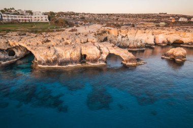 Denizin üzerindeki doğal bir kaya kemerinin nefes kesici görüntüsü, sakin suları yansıtan parlak bir günbatımı..