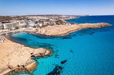 Kıbrıs Rum Kesimi 'nin Aya Napa kentindeki turkuaz suların ve kumlu plajların yer aldığı tropikal bir kıyı şeridinin çarpıcı hava manzarası.