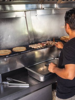 Bir şef paslanmaz çelik ızgarada ızgara şiş ve yassı ekmek pişiriyor, profesyonel mutfak ortamında geleneksel pişirme tekniklerini sergiliyor. Limasol, Kıbrıs - 27 Ekim 2024.