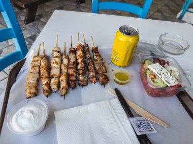 Izgara et şişleri, feta peynirli Yunan salatası, tzatziki sosu, zeytinyağı ve masada servis edilen ferahlatıcı bir konserve içeceğin yer aldığı lezzetli bir yemek. Limasol, Kıbrıs - 27 Ekim 2024.