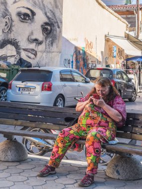 A relaxed street view featuring a woman on a bench, vibrant graffiti artwork, parked cars, and hanging lights add charm to the urban atmosphere. Nicosia, Cyprus - October 26, 2024. clipart