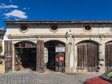 Ahşap kapılar, dairesel pencereler ve yıpranmış bir taş cephe bulunan eski atölye, güneşli bir gökyüzünün altında bir kaldırım taşı caddesinde yer alıyor. Larnaca, Kıbrıs - 23 Ekim 2024.