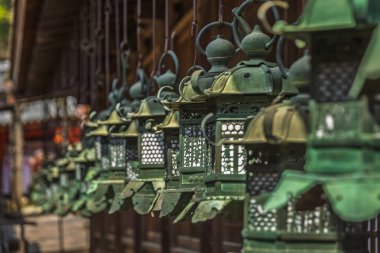 Bir Japon tapınağında asılı antik bronz fenerlerle dolu sıra. Karmaşık detaylar ve geleneksel işçilik sergiliyor. Bu yıpranmış fenerler kutsal mekana huzurlu bir atmosfer ekler..