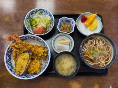Lezzetli bir Japon Ten Don seti siyah bir tepside servis edilir. Tempura, karides, patlıcan, pilav, udon eriştesi, miso çorbası, salata, turşu ve meyve içerir. Bu lezzetli ve sağlıklı yemeğin tadını çıkarın..