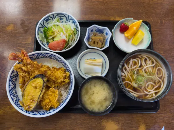 Lezzetli bir Japon Ten Don seti siyah bir tepside servis edilir. Tempura, karides, patlıcan, pilav, udon eriştesi, miso çorbası, salata, turşu ve meyve içerir. Bu lezzetli ve sağlıklı yemeğin tadını çıkarın..