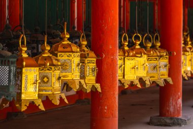 Japonya 'nın Kyoto kentindeki canlı bir kırmızı tapınağın tavanında asılı karmaşık altın fenerler. Süslü detaylar ve zengin renkler dingin ve büyüleyici bir sahne yaratır..