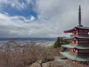 Japonya Chureito Pagoda 'dan Fujiyoshida şehrinin panoramik manzarası. Büyüleyici kırmızı bir pagoda, ilkbahar çiçeklerinin erken açtığı bir şehir manzarasına bakar. Dramatik bulutlar derinlik ekler.