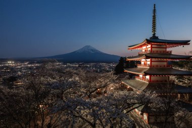 Fuji Dağı 'nın Fujiyoshida, Japonya' daki Chureito Pagoda 'dan gece manzarası, kiraz çiçeği mevsiminde. Göz kamaştırıcı dağ ve şehrin ışıklarıyla aydınlatılmış tapınak..