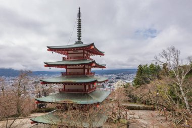 Hakone, Japonya 'ya bakan göz kamaştırıcı kırmızı pagoda. Ön planda kiraz çiçekleri şehir manzarasına ve dağ zeminine canlı bir renk ekler. Resimli bir bahar sahnesi.