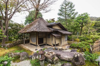 Sazdan çatılı, sakin bahçeli geleneksel Japon evi. Taş fenerler ve yosun kaplı kayalar sakin atmosferi geliştirir. Kyoto, Japonya.
