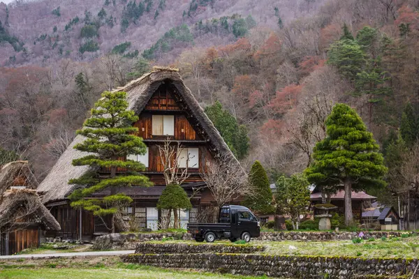 Shirakawa-go, Japonya 'da park etmiş küçük bir kamyoneti olan geleneksel bir ev. İkonik sazdan çatı ve çevreleyen dağ manzarası huzur verici bir manzara yaratır..