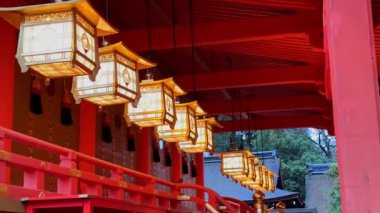 Illuminated lanterns hang in a row at Fushimi Inari-taisha Shrine in Kyoto, Japan. The warm light contrasts beautifully with the vibrant red architecture. A captivating scene of Japanese culture and