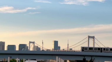 Gökkuşağı Köprüsü ve Tokyo Kulesi uzaktayken gün batımında Tokyos şehrinden geçen yükseltilmiş tren. Huzurlu bir şehir manzarası. Huzurlu bir arka plana karşı modern ulaşım sergileniyor..