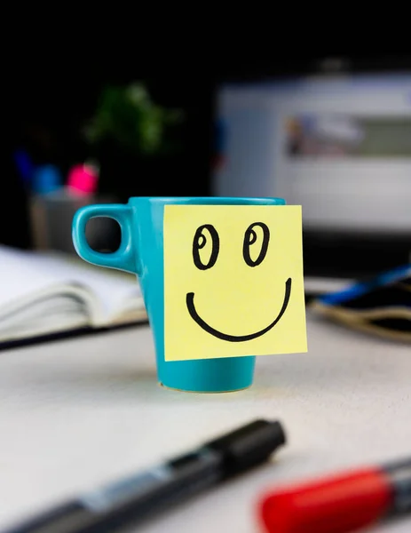 Stock image Smiling face drawn on sticky note on a cup of coffee at the office desk. Every morning wake up with the smile