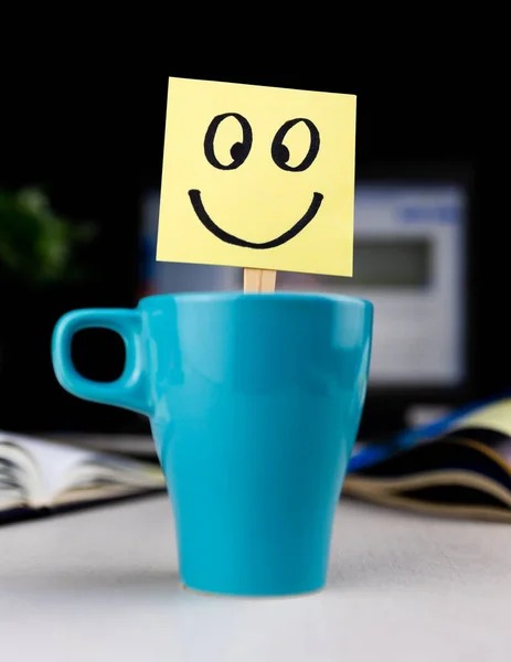 stock image Smiling face drawn on sticky note inside a cup of coffee at the office desk. Every morning wake up with the smile