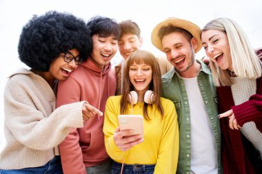 Bir grup neşeli genç cep telefonundan komik bir şey izliyor. Heyecanlı öğrenciler cep telefonu teknolojilerini kullanıyorlar. Gençlik kavramı, arkadaşlık, uygulama, hipster, milenyum. Yüksek