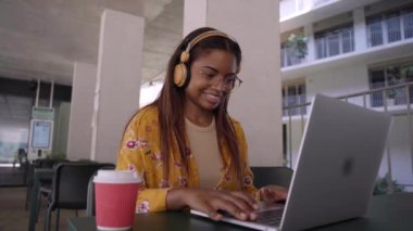 Genç siyahi Afrikalı kadın üniversite öğrencisi dizüstü bilgisayar kullanarak online öğreniyor. Gülümseyen kız Webinar 'ı ya da sanal eğitim uzaktan eğitim kursunu izliyor dışarıda çalışıyor kampüs alanının dışında oturuyor..