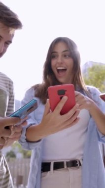 Dikey video. Bir grup genç ellerinde cep telefonlarıyla ekrandan komik bir şey izliyorlar. Akıllı telefona benzeyen şaşırmış yüzler. Teknoloji bağlantı topluluğu ve sosyal medya kavramı 