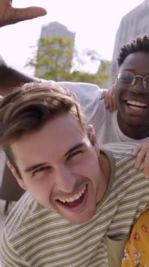 Happy Young 'ın kameraya bakıp güldüğü dikey bir video. Gülümseyen bir grup insan dışarıda eğleniyor. Öğrenci birliği. Çok kültürlü insanların yaşam tarzı neşeli..